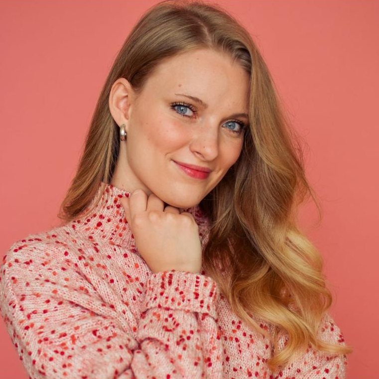 Paige McKenna headshot, hand at chin, speckled pink sweater on a coral backdrop