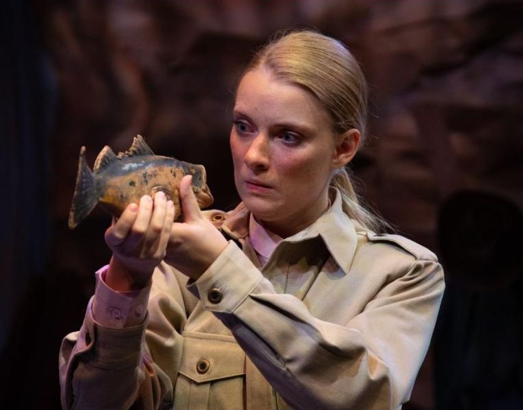 Paige as Frank Goodman in a khaki expedition shirt, examining a fish